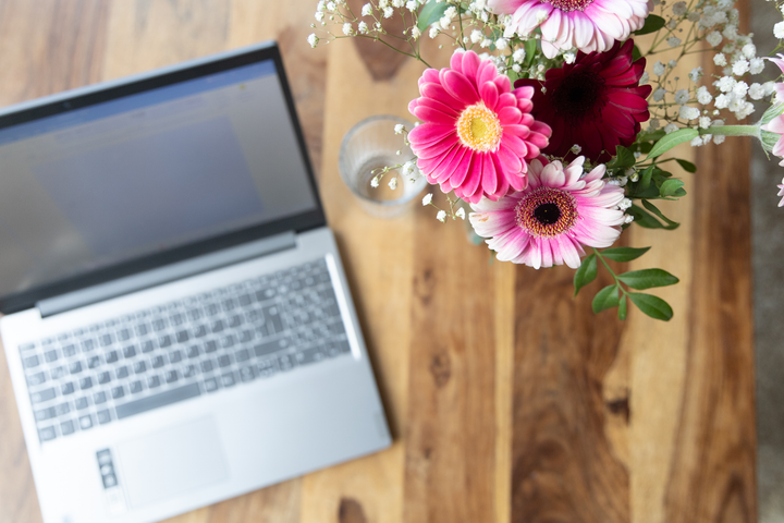 Offener Laptop und Blumen auf einem Holztisch